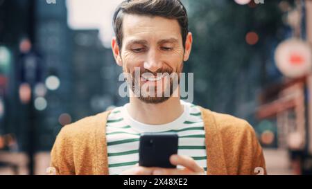 Kaukasier benutzt Smartphone in der Großstadt. Kreativer Profi mit Mobile Phone App für E-Commerce-Investitionen, Online-Shopping, soziale Medien und Surfen im Internet. Porträt Aufgenommen. Stockfoto