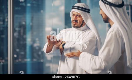 Zwei erfolgreiche muslimische Geschäftsleute in weißem Traditional Outfit, die im Büro sitzen, verhandeln und über finanzielle Chancen sprechen. Saudi, Emirat, Arabisches Geschäftsmann-Konzept. Stockfoto