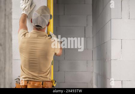 Kaukasischer professioneller Maurerarbeiter, der mit dem Wasserwaage-Tool die Füllstände überprüft Stockfoto