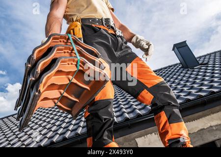 Kaukasischer Dachdecker, der eine schwarze Dachkeramikfliese entlang der Baustelle bewegt Stockfoto