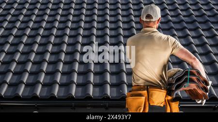 Professioneller Kaukasischer Dachdecker, der eine schwarze Dachkeramik in seinen Händen bewegt Stockfoto