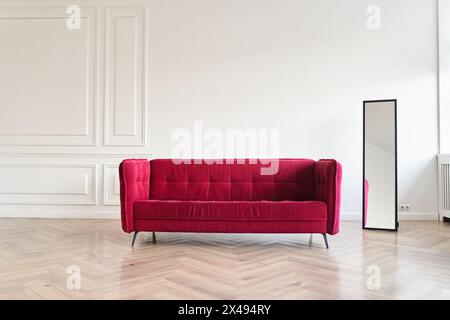 Das Interieur ist in einem minimalistischen klassischen Stil gehalten. Moderne Inneneinrichtung für Handwerker im Wohnzimmer mit rotem Sofa, Spiegel und Kopierraum für Ihr Design mit leerer Wand für Poster. Hohe Qualität Stockfoto