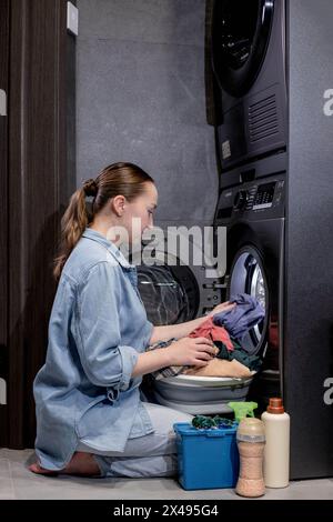 Die junge Frau nimmt die gewaschenen Kleider zu Hause aus der Waschmaschine. Stockfoto