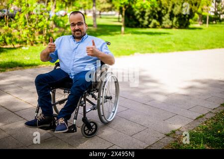 Porträt des glücklichen Mannes im Rollstuhl. Er genießt einen sonnigen Tag im Stadtpark. Stockfoto