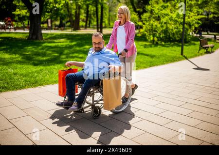 Ein Mann im Rollstuhl geht vom Einkaufen. Sein Freund hilft ihm beim Rollstuhl. Stockfoto