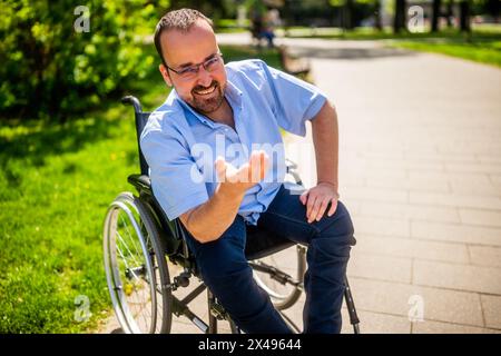 Porträt des glücklichen Mannes im Rollstuhl. Er genießt einen sonnigen Tag im Stadtpark. Stockfoto