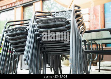 Die Stühle wurden von einer geschlossenen Bar-Terrasse gesammelt. Gestapelte Stühle auf der Veranda des Cafés Stockfoto