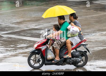 SAMUT PRAKAN, THAILAND, 20. März 2024, Eine Familie mit Regenschirmen fährt im Regen mit dem Fahrrad Stockfoto