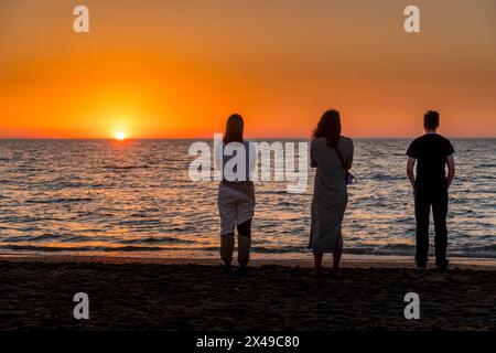 Drei Personen beobachten den Sonnenaufgang am Sandstrand in der Hauptstadt der Republik Dagestan im Süden Russlands Stockfoto