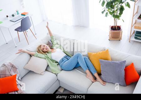 Foto von positiver guter Laune Mädchen auf der Couch mit erhobenen Händen kaufen Immobilien eigenes Haus genießen Komfort zu Hause Stockfoto