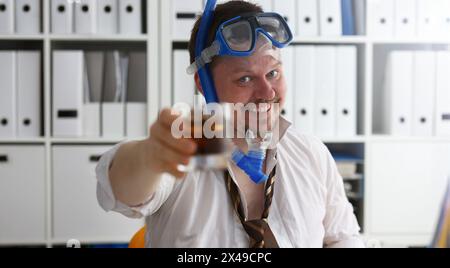 Mann, der Anzug und Krawatte in einer Brille trägt und Schnorchelgriff in einem Armglas Cola am Arbeitsplatz in der Büronähe. Anzahl der Tage, um den jährlichen Tag frei von Workaholi zu lassen Stockfoto