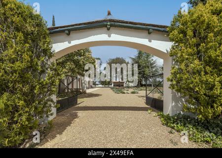 Eingangsbogen im Umkreis eines Landhauses im andalusischen Stil mit weißen Wänden, Kieswegen und einer Vielzahl von Bäumen Stockfoto