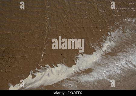 Ein Strand mit einer Schaum-Welle auf dem Sand. Der Schaum ist weiß und er kommt vom Meer Stockfoto