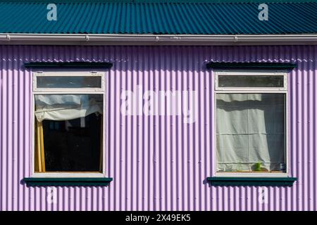 Das Haus hat ein blaues Dach und violette Wände. Die Fenster sind offen und die Vorhänge sind gezeichnet Stockfoto