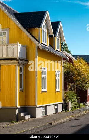 Ein gelbes Haus mit schwarzem Dach und weißer Verkleidung. Das Haus ist von Bäumen umgeben und hat eine Veranda Stockfoto