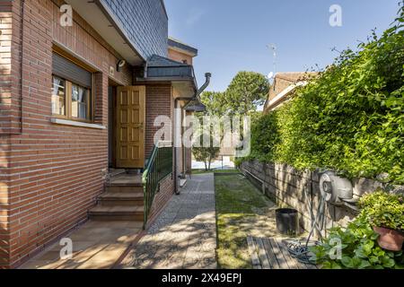 Umkreis-Garten mit gekacheltem Weg um ein freistehendes Haus mit Ziegelfassaden mit Schläuchen und Zugang mit Treppe und Geländer Stockfoto