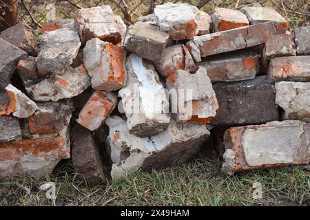 Ein Haufen gebrochener alter Ziegelsteine, der vor einem Maschendrahtzaun liegt. Stockfoto