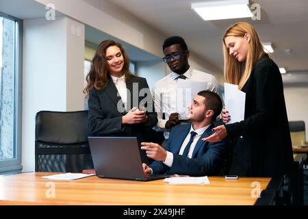 Multiethnische Geschäftsteams arbeiten in modernen Büros zusammen. Afrikanische, arabische und kaukasische Fachleute diskutieren über Strategie, feiern Erfolge rund um Laptop Stockfoto