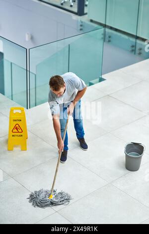 Mann, Hausmeister und wischen den Büroboden ab oder reinigen Sie Hygiene mit Vorsicht oder Wasser, Seife oder Bakterien. Männliche Person, Desinfektion und Firma Stockfoto