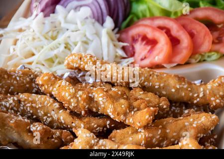 Sesam-beschichtete gebratene Streifen, serviert mit frischem Salat auf einem Essenstablett. Stockfoto