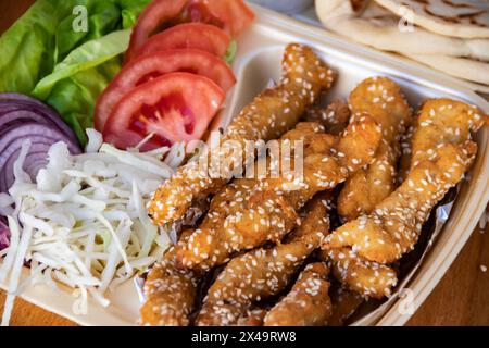 Sesam-beschichtete gebratene Streifen, serviert mit frischem Salat auf einem Essenstablett. Stockfoto