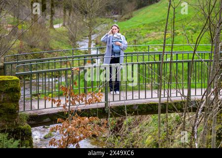 Gestresste, erschöpfte und depressive Frau, die mit ihrem kleinen Baby auf einer Brücke in der Natur steht Stockfoto