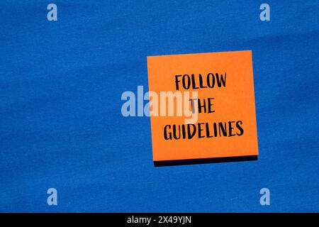 Befolgen Sie die Anweisungen auf einem orangefarbenen Papieraufkleber mit blauem Hintergrund. Konzeptionell Befolgen Sie das Richtliniensymbol. Kopierbereich. Stockfoto