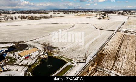 Ein Blick aus der Vogelperspektive auf Eine frostige Landschaft mit Teich, Eisenbahn und schneebedeckten Feldern. Stockfoto