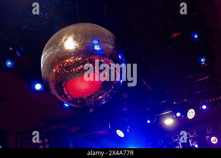 Klassische große Discokugel aus kleinen Spiegeln, die helle und warme Lichter an der Decke eines Nachtclubs oder Konzertsaals reflektieren. Die Tanzfläche kann sein Stockfoto