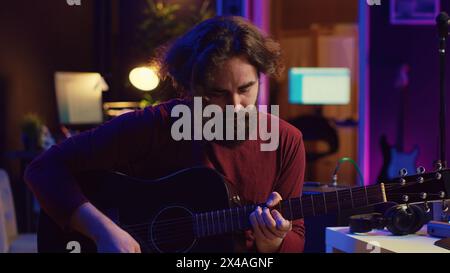 Junger Mann, der Gitarre spielt und Musik mit der Equalizer daw Software-Schnittstelle kreiert. Musikproduzent nimmt im Heimstudio einen Song auf und mischt akustische Klänge auf der Stereo-Konsole. Kamera A.. Stockfoto