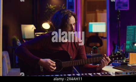 Junger Songwriter, der Gitarre spielt und Musik mit Equalizer-Programm kreiert. Musiker, der Songs im Heimstudio aufnimmt, Ingenieur mischt und meistert Pop-Rock-Tracks. Kamera A.. Stockfoto