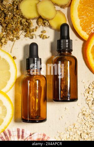 Zwei braune Flaschen ätherischen Öls mit Tropfer auf einer natürlichen Baumwolloberfläche und umgeben von den Zutaten des Öls: Frische Orange, Zitrone und Stockfoto