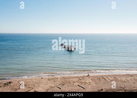 Ruhige Strandszene mit Schiffswrack in ruhigen Gewässern, klarem blauem Himmel Stockfoto