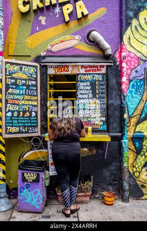 Eine junge Frau bestellt Essen in Einem farbenfrohen Takeaway Café in der Stadt Valparaiso, Region Valparaiso, Chile. Stockfoto
