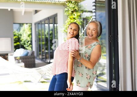 Asiatische Großmutter und birassische Teenager-Enkelin lächeln zu Hause zusammen, Kopierraum. Großmutter zeigt kurze graue Haare, Enkelin-Flauntin Stockfoto