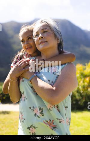 Asiatische Großmutter und birassische Teenager-Enkelin, die sich draußen umarmt. Beide tragen dunkles Haar, eine junge Frau zeigt ein warmes Lächeln und teilt freudige Momente Stockfoto