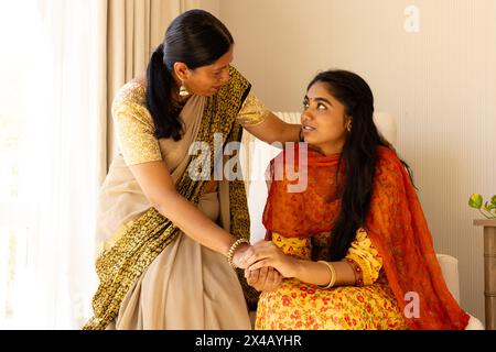Indische Mutter in sari tröstender Teenager-Tochter, beide in traditioneller Kleidung. Mutter mit schwarzem Haar, Tochter mit braunen Augen, genießt einen ruhigen Moment Stockfoto