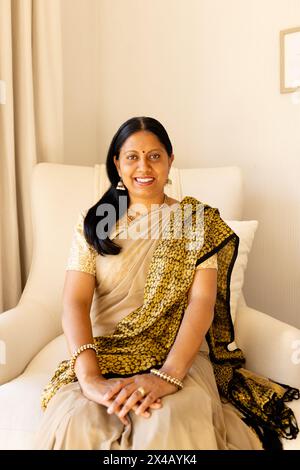 Indianerin in traditioneller indischer Kleidung, sitzt zu Hause. Sie hat dunkles Haar und reife Haut, zeigt ein warmes Lächeln, genießt eine friedliche Mutter Stockfoto