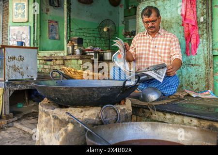 Der Besitzer eines Lebensmittelgeschäfts liest eine Zeitung in Varanasi, Indien. Stockfoto