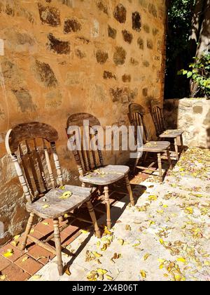 Vier alte Holzstühle an einer Steinmauer. Außenwand aus verwittertem Stein des Gebäudes Stockfoto