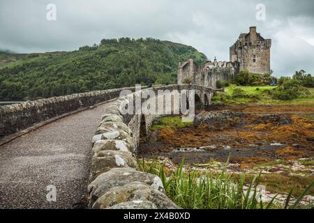 Nahaufnahme der Brücke über den Fluss, die zum Eilean Donan Castle in Schottland führt. Das Schloss ist von einer üppigen Landschaft umgeben. Stockfoto