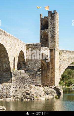 Die mittelalterliche Brücke von Besalú, Girona, mit einem ihrer Türme mit zwei Fahnen oben. Die Brücke führt über den Fluss Fluvià. Stockfoto