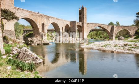 Die malerische mittelalterliche Brücke von Besalú in Girona überquert den Fluss Fluvià, der sich im Wasser spiegelt. Die Brücke ist alt und hat eine Steinstruktur. Stockfoto