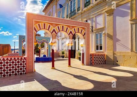 Blick auf Silves Stadtgebäude mit einem rot-weißen Torbogen und einem blauen Brunnen, Algarve Region, Portugal. Stockfoto