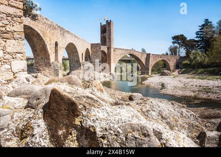 Die mittelalterliche Brücke von Besalú überquert den Fluss Fluvià mit einer Steinmauer auf beiden Seiten. Die Brücke ist alt und hat ein rustikales Aussehen. Stockfoto