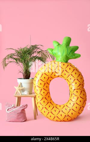 Aufblasbarer Ring in Form von Ananas, Zimmerpflanze und Beutel auf rosa Hintergrund Stockfoto