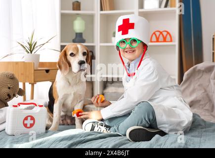 Niedlicher kleiner Arzt, der den Blutdruck des Hundes mit Spielzeug im Schlafzimmer misst Stockfoto