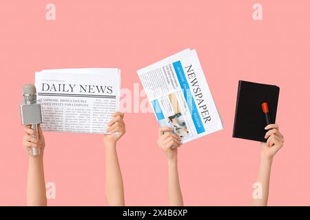 Weibliche Hände mit Zeitungen, Notizbuch und Mikrofon auf rosa Hintergrund Stockfoto