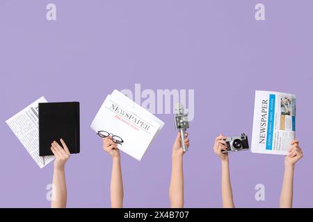 Weibliche Hände mit Zeitungen, Fotokamera, Notebook und Mikrofon auf Fliederhintergrund Stockfoto