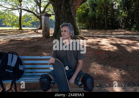 Brasilianischer Skateboarder über 50 Jahre, der sich auf einer Bank in einem Quadrat entspannt 1. Stockfoto